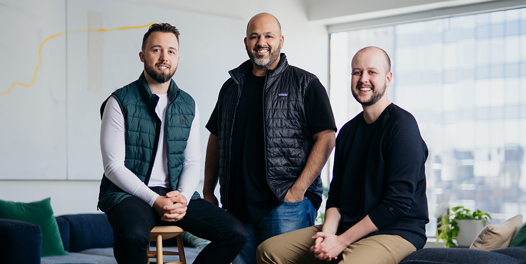 Three smiling co-founders of OneVest, in casual business attire, pose confidently in their modern, sunlit office